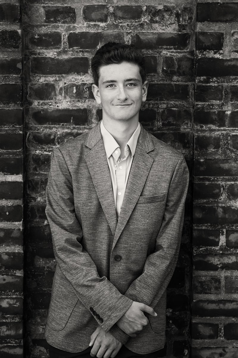 teenage male wearing suit in front of brick wall