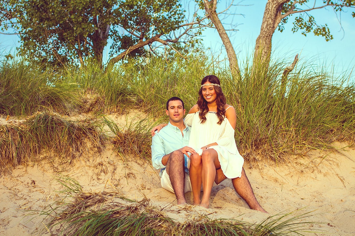 couple sitting together on beach with tall grasses behind