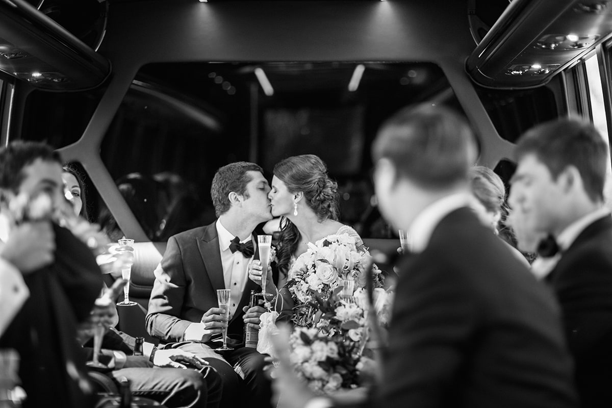 newly married couple kissing and riding in limousine with wedding party